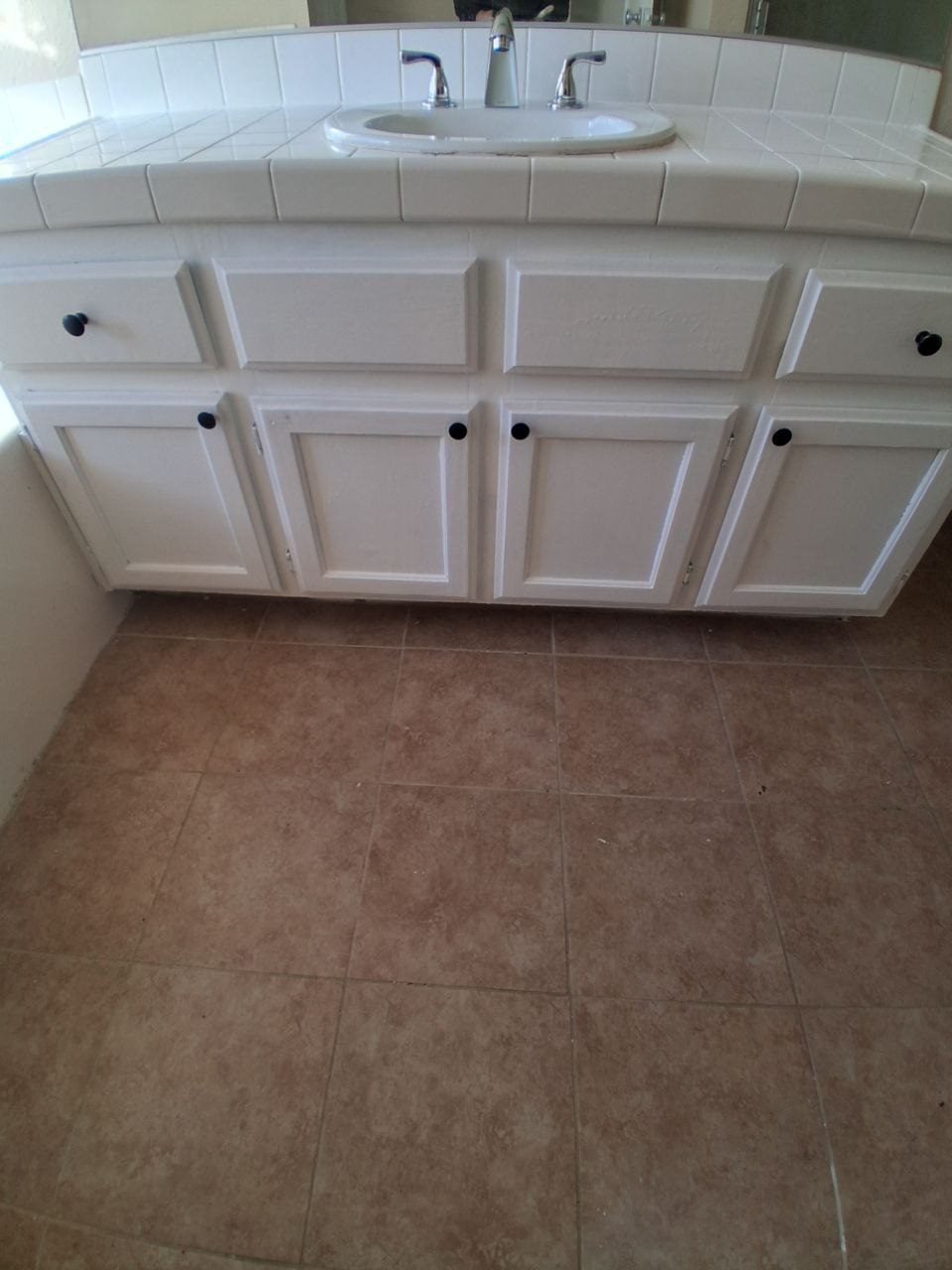 White bathroom vanity with a tiled top over a tile floor